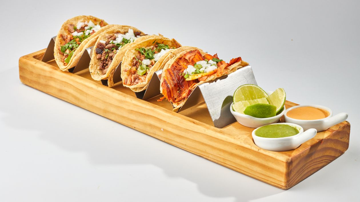 Colorful variety of Mexican street tacos with lime and salsas on a wooden tray