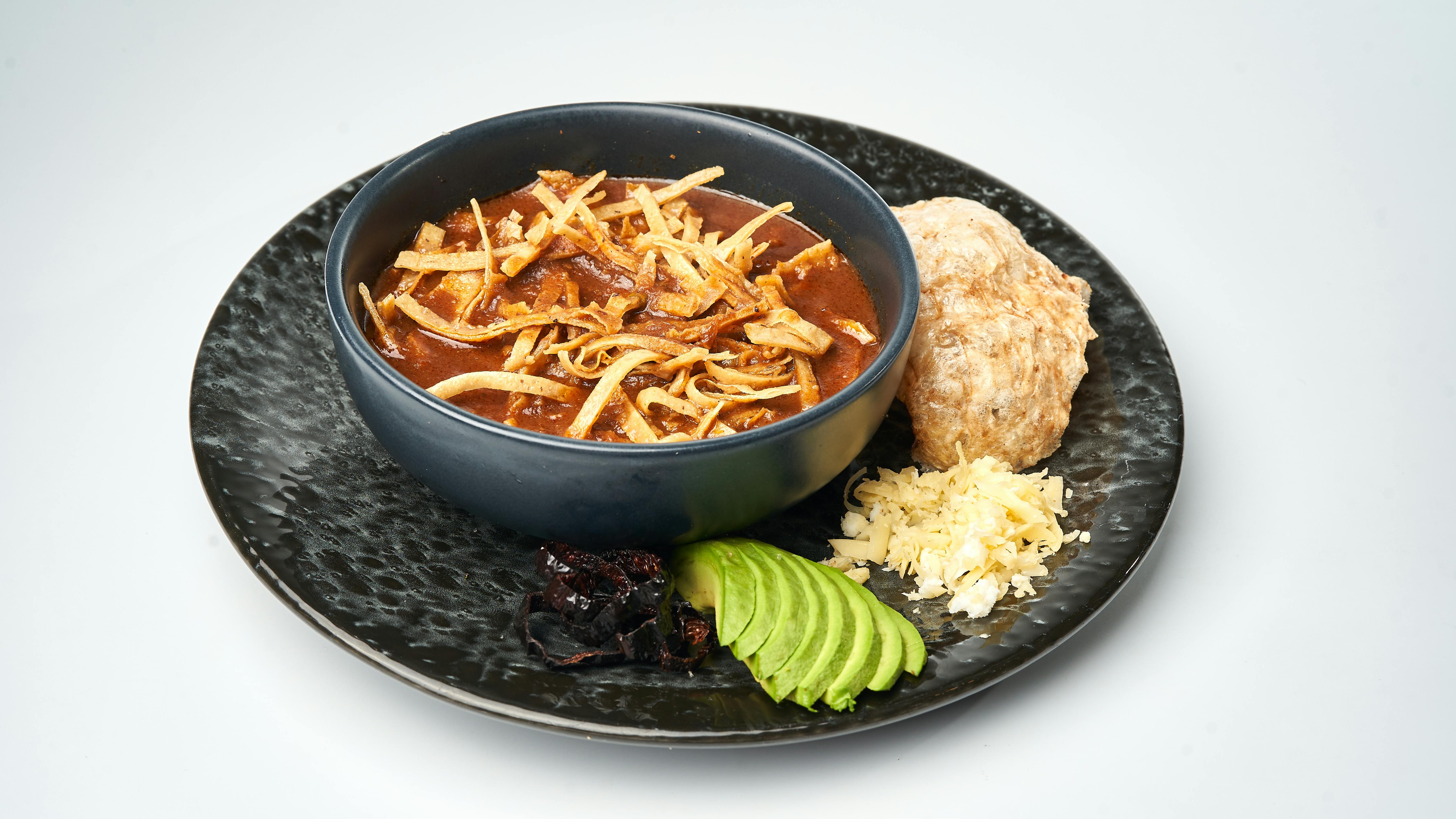 Chicken Tortilla Soup With Garnishes Of Fried Tortilla Strips, Avocado, And Cheese