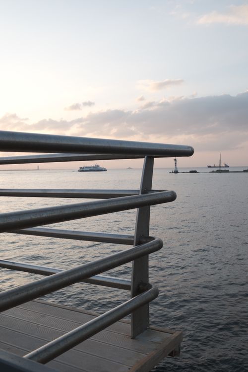 Free Serene ocean view from a pier at sunset with boats in the distance under a pastel sky. Stock Photo