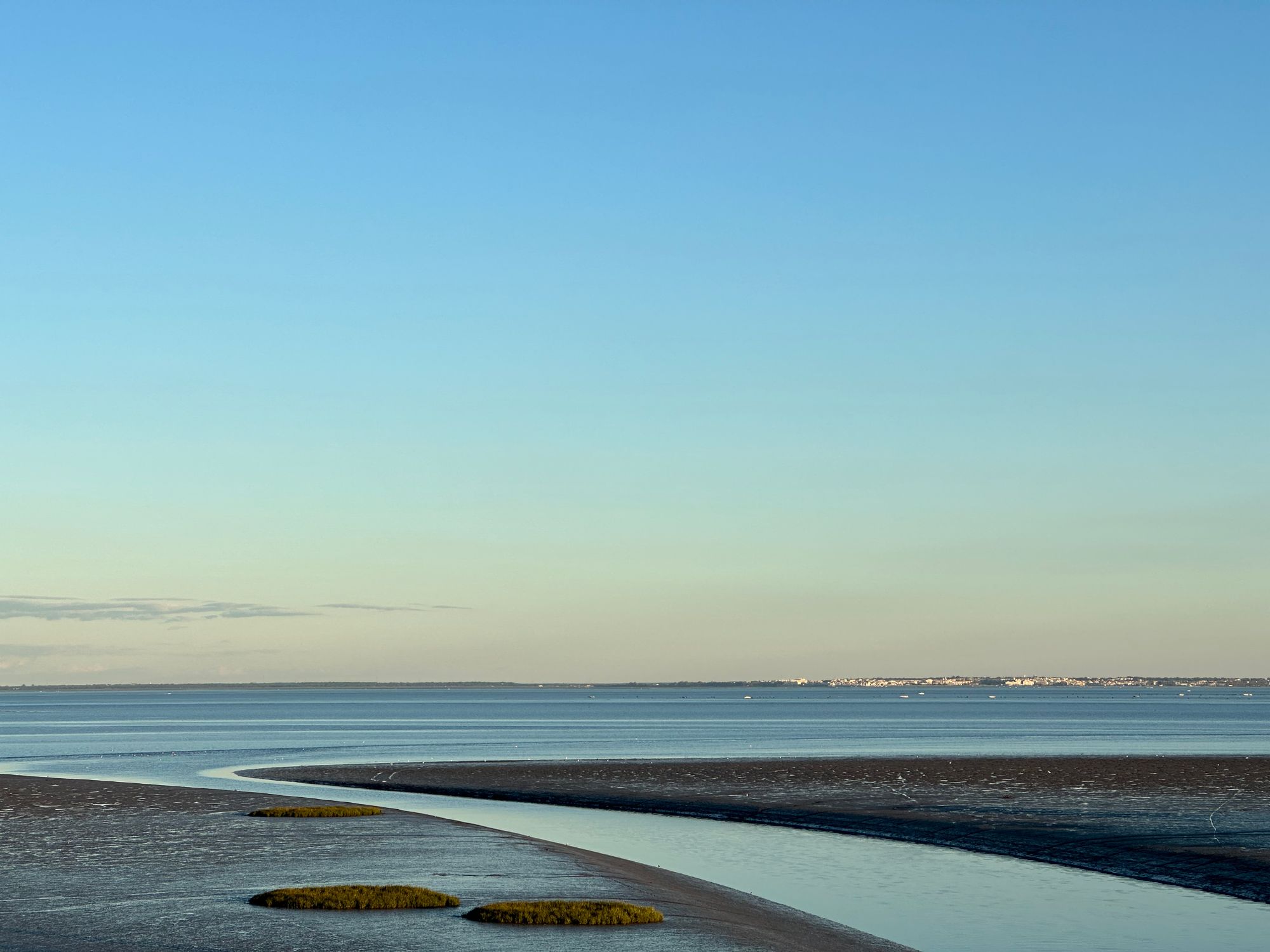Agua poco profunda en la orilla de un estuario, con la línea de costa al fondo