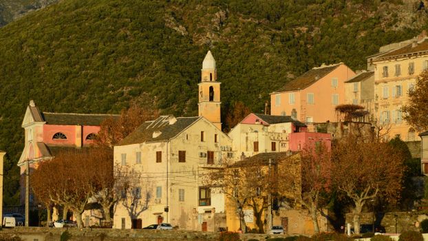 Picturesque view of Nonza village with traditional Corsican architecture against a lush hillside in autumn.