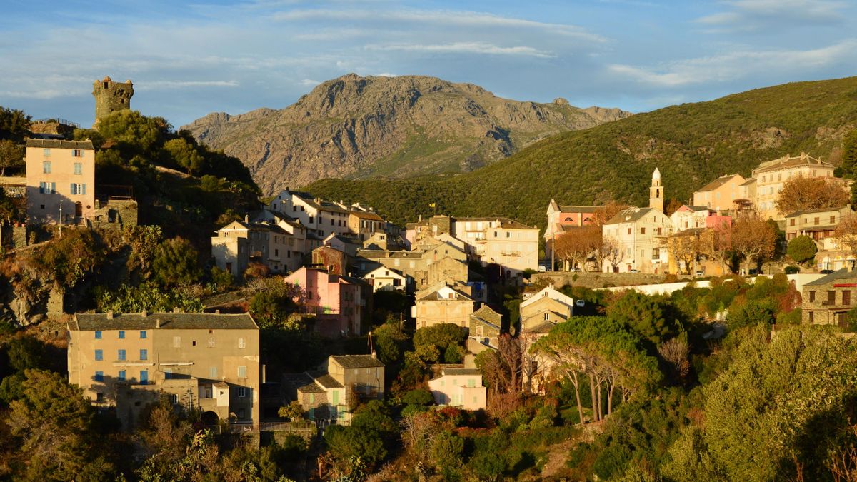 Nonza village and its Genoese tower above the sea with mountains at sunset