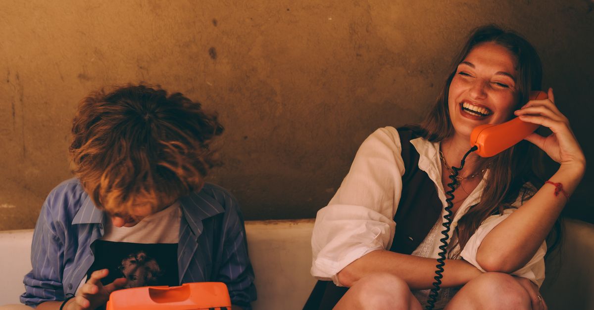 Young people sitting in a circle, laughing, with laptops and phones scattered around them, natural lighting