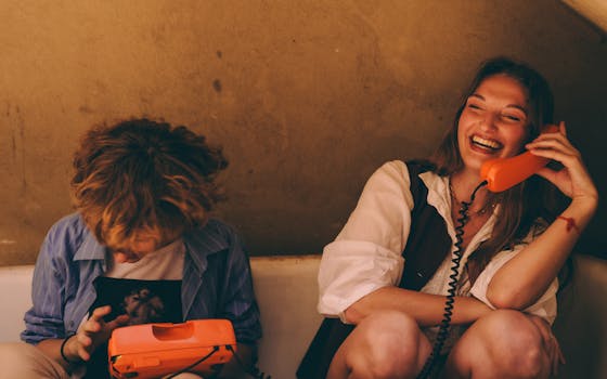 Two young adults enjoying a lively conversation on vintage orange corded phones indoors.