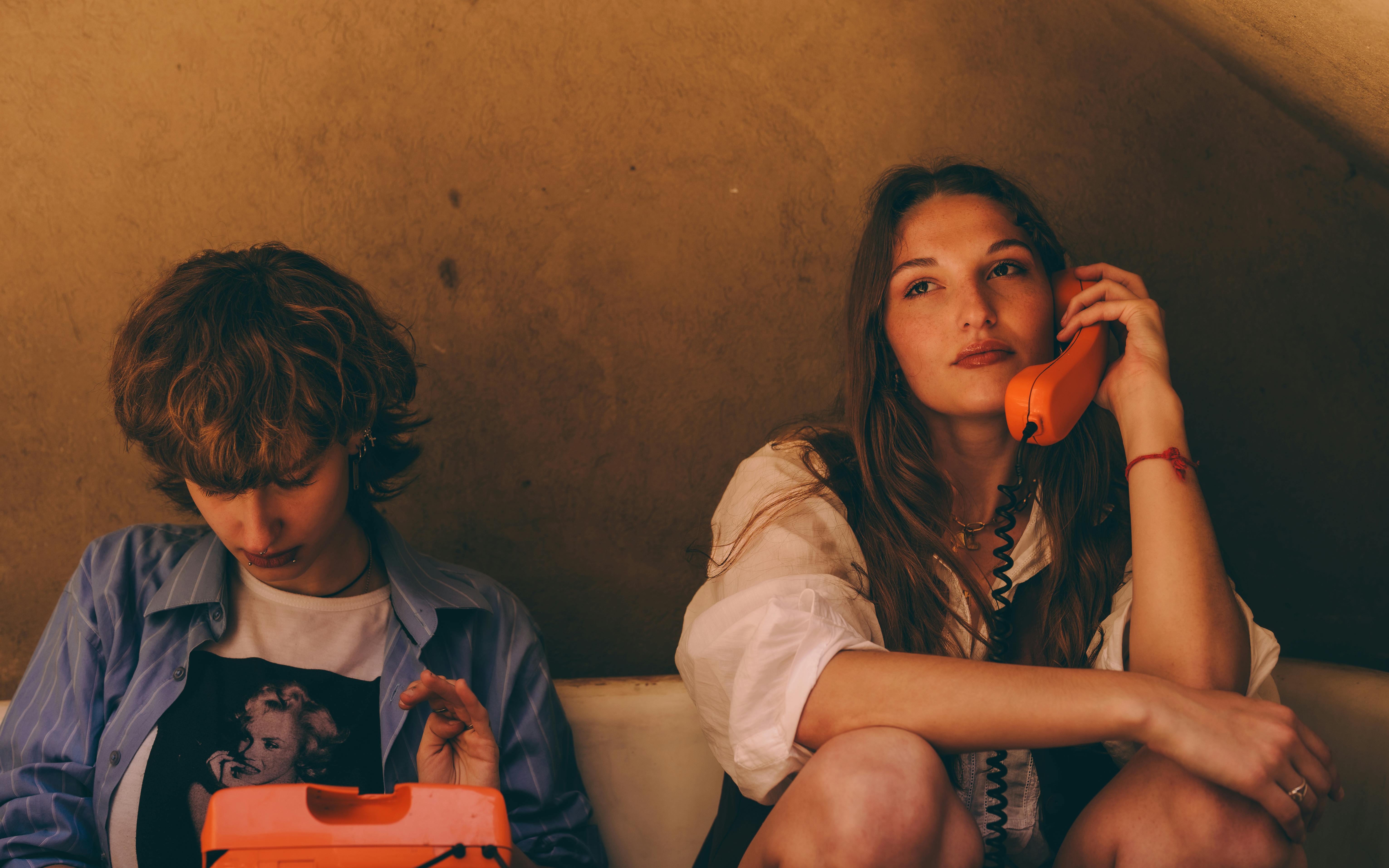 De franc Dos adolescents en un ambient retro utilitzant un telèfon vintage taronja. Foto d'estoc