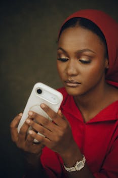 Portrait of a woman in red clothing focused on her smartphone screen indoors.