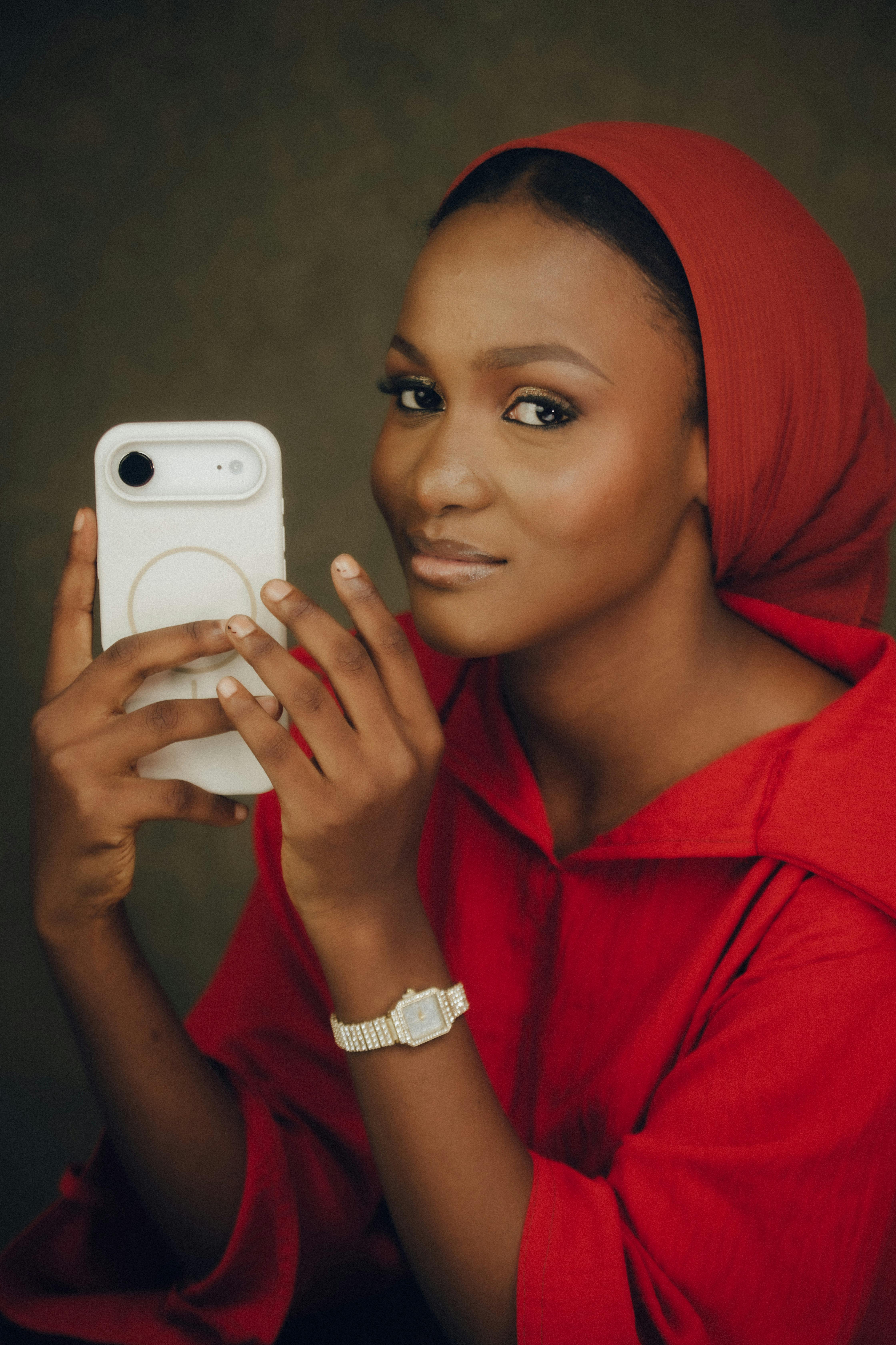 Portrait of a woman in a red hijab using a smartphone for a selfie indoors.