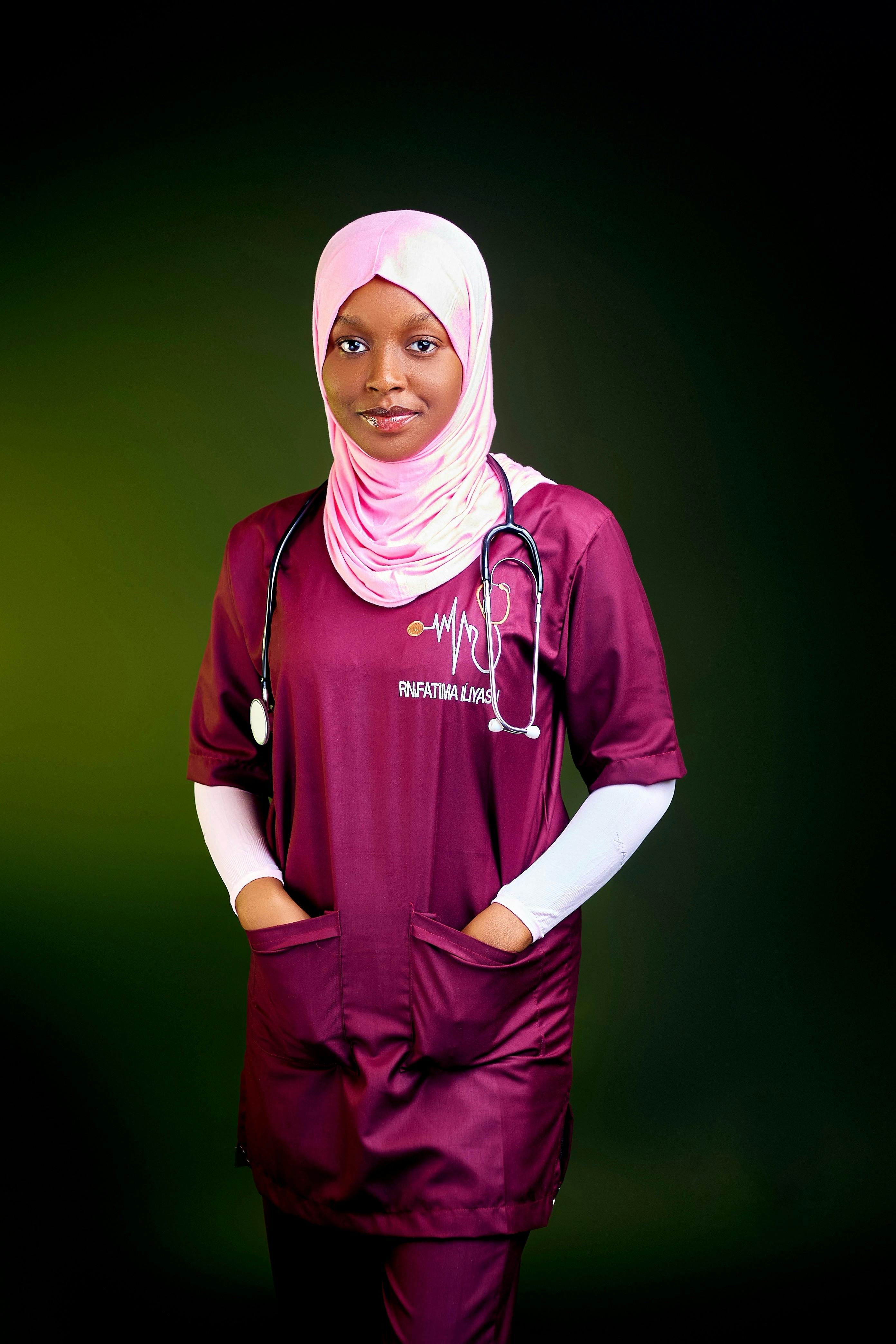 Young medical professional in maroon scrubs and hijab, confidently posed.
