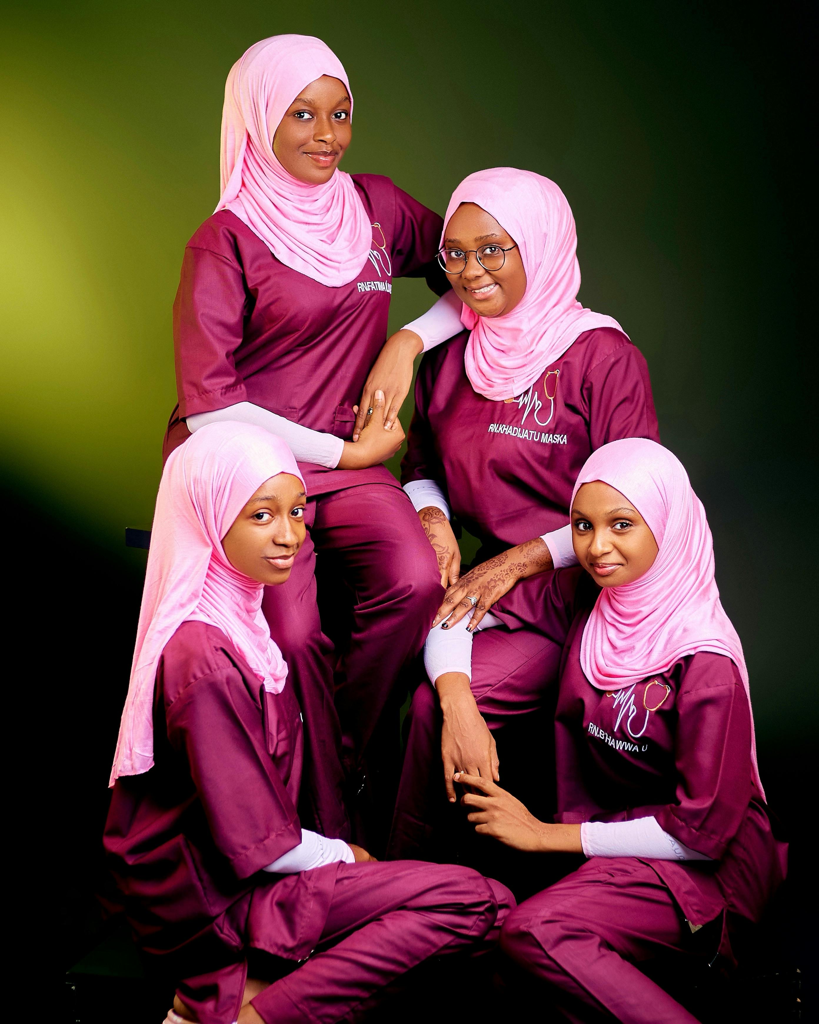 Four women in matching hijabs and burgundy outfits pose with a friendly demeanor.