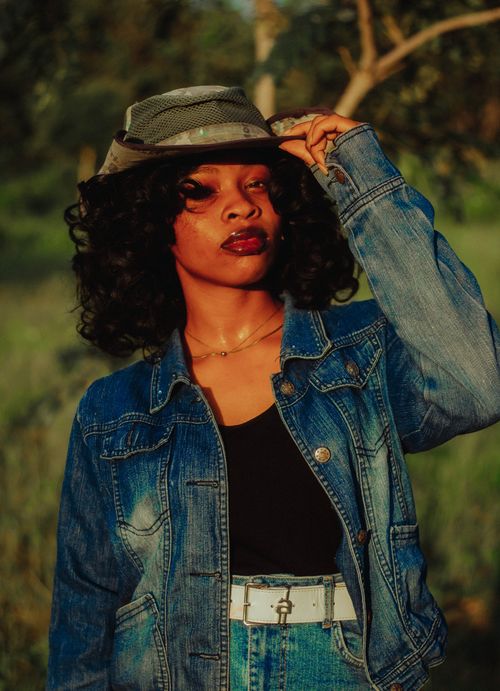 Free Fashionable woman in denim and hat posing stylishly in a sunny outdoor setting. Stock Photo