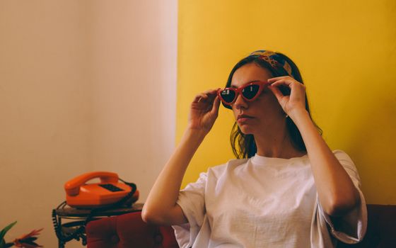 Stylish woman in red sunglasses with phone, vintage vibe indoors.