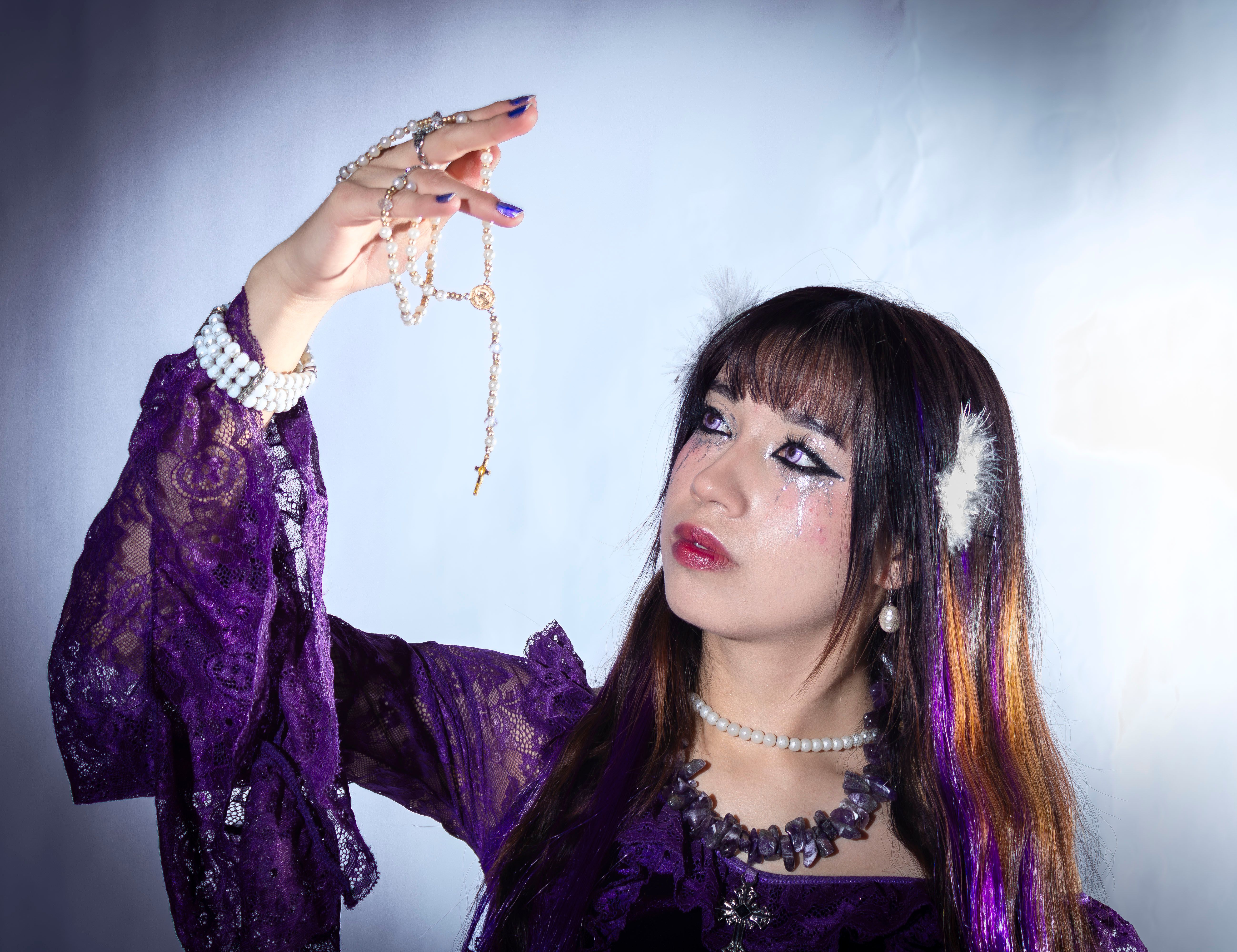 Glamorous woman in elegant purple dress holding a rosary, exuding grace and style.