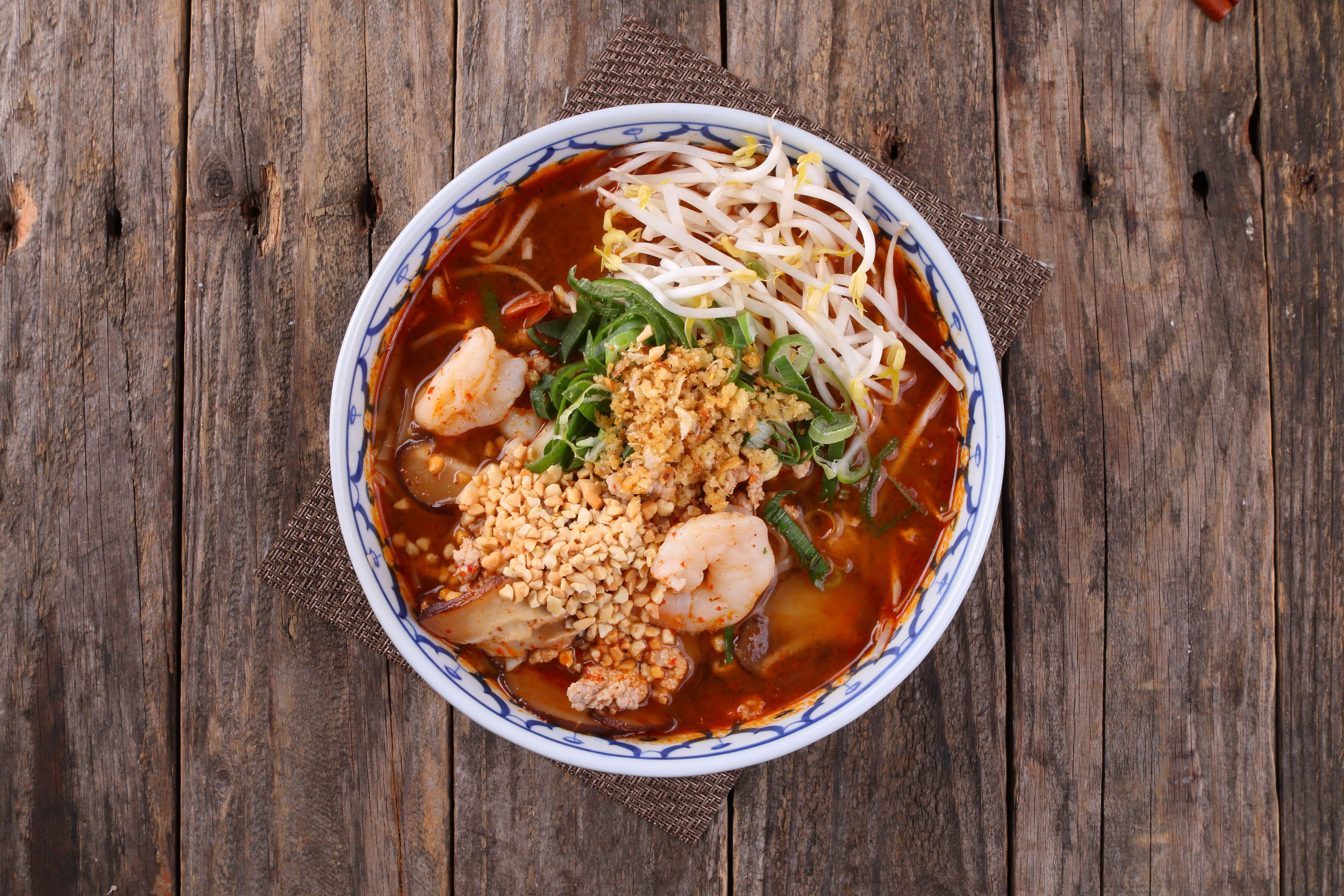 Top-down view of a vibrant shrimp noodle soup with garnish on a rustic wooden table.