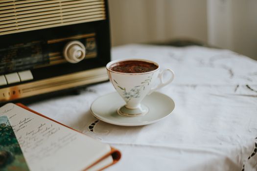 A vintage scene featuring a teacup of coffee, retro radio, and open notebook.