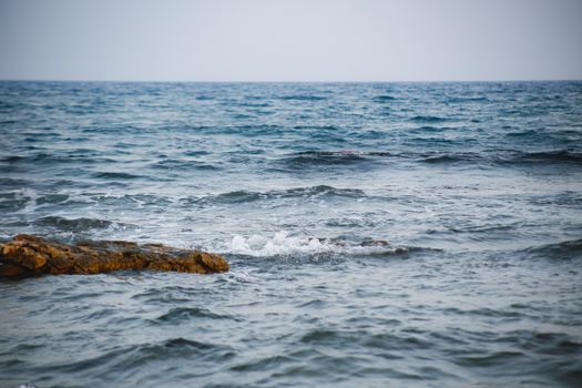 Calming view of ocean waves gently hitting a rocky shoreline under a clear sky.