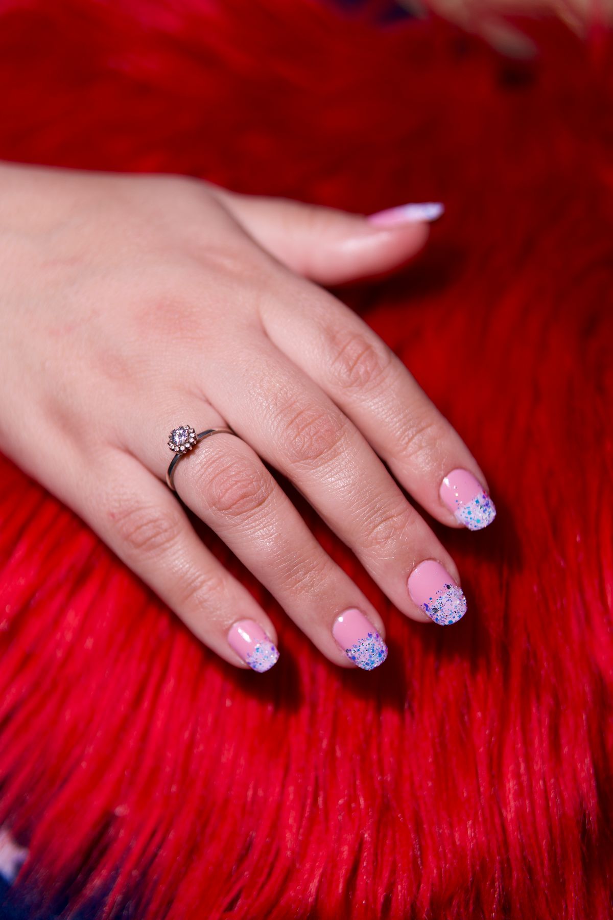 Close-up of a manicured hand with ring, nail art design on a vibrant red fur background.