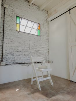 Bright minimalist room with a white chair, book, and stained glass window in Buenos Aires.