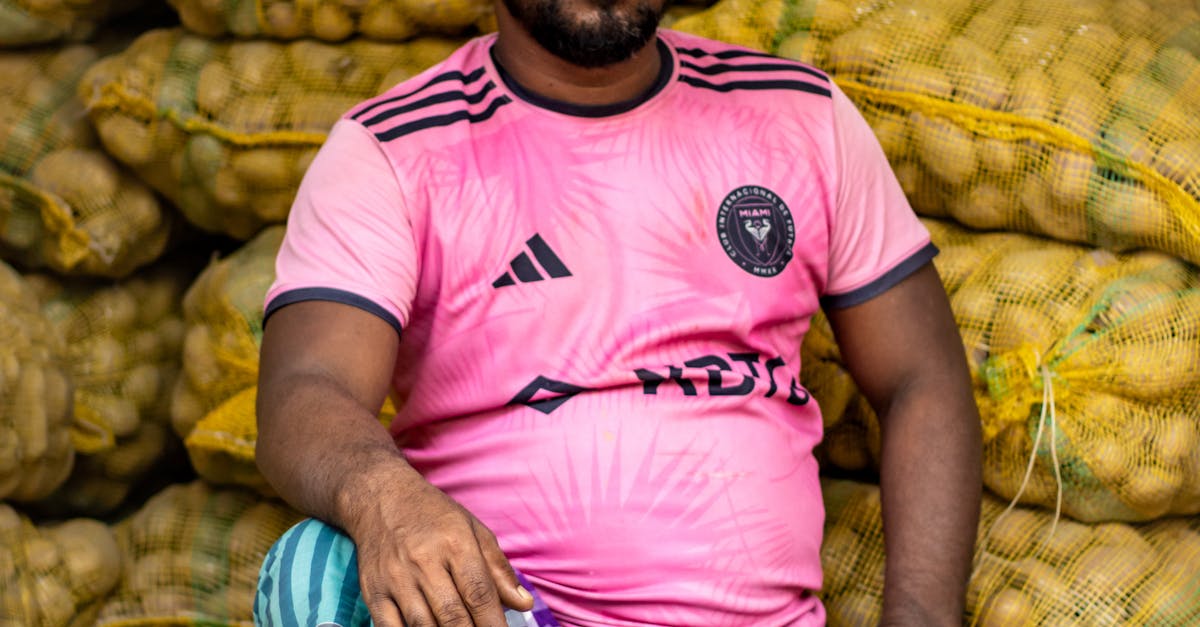 Photo by Abir Hasan A man sits with bags of potatoes, wearing a pink sports jersey in a market setting.