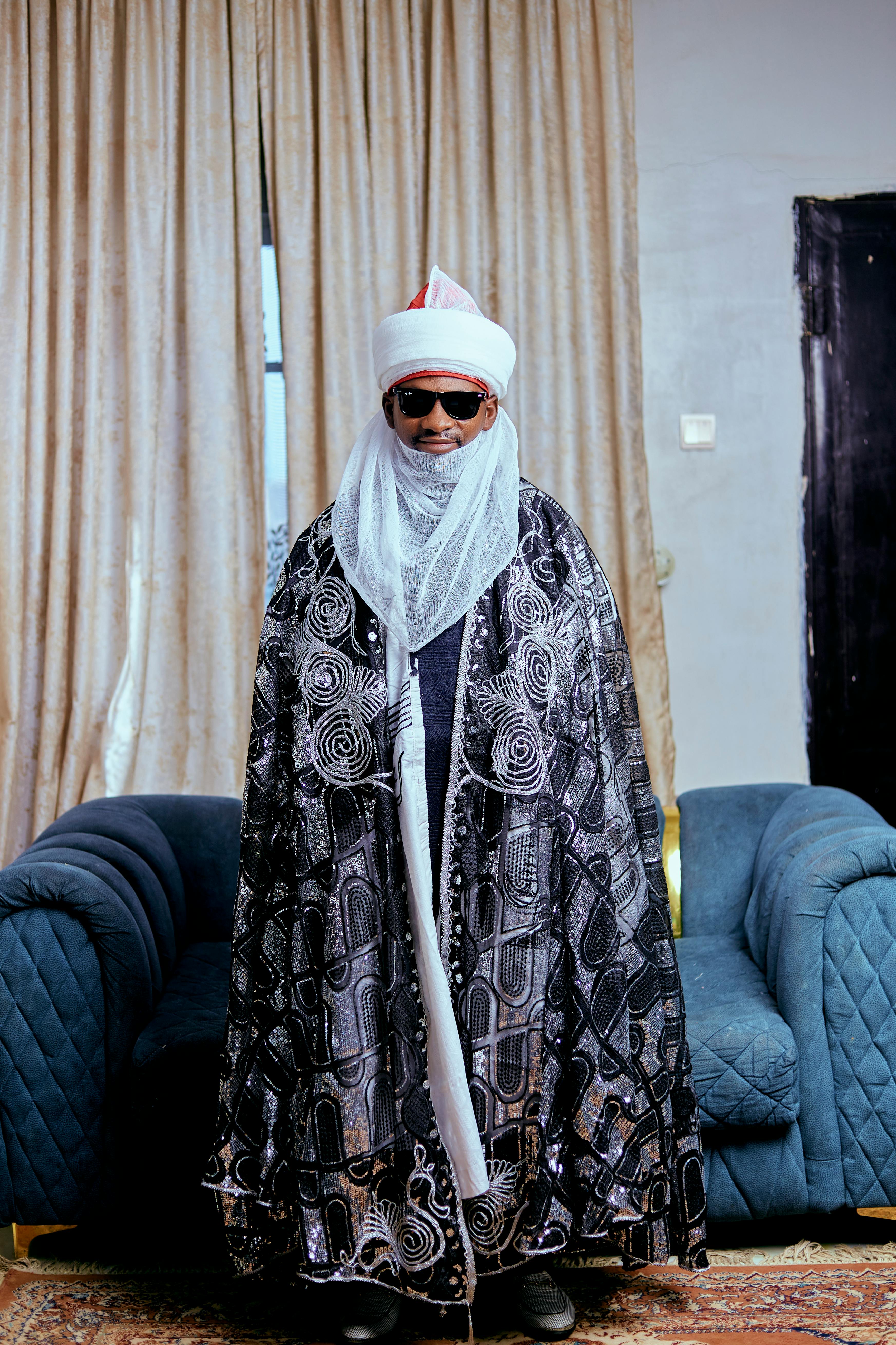 grátis Homem vestindo trajes tradicionais e óculos de sol, em ambiente interno, exibindo elegância cultural. Foto profissional