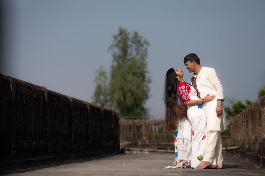 A couple embraces outdoors in traditional attire in West Bengal, India.
