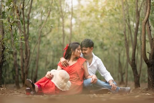 Free A loving couple in a red dress and white shirt share a tender moment in a lush forest setting. Stock Photo