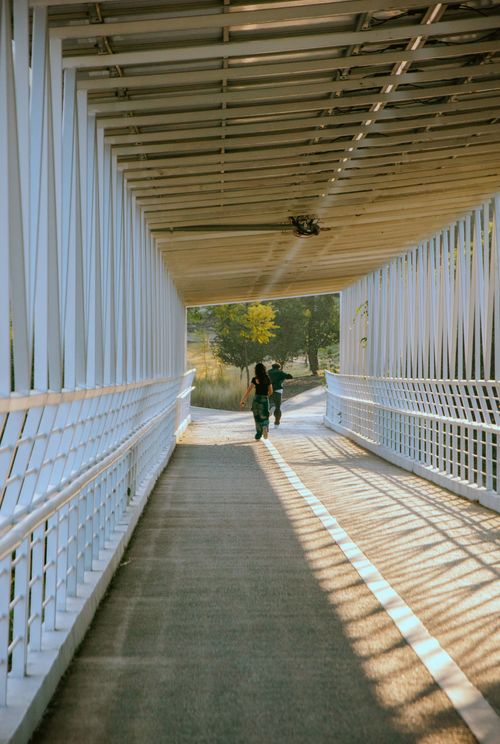 Free A couple walks through a modern pedestrian bridge, enjoying a sunny outdoor stroll. Stock Photo