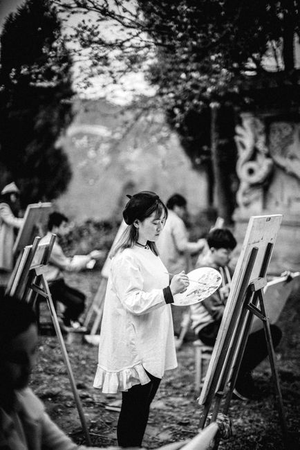 A group of young artists paint outdoors in a monochrome setting, capturing creativity and leisure.