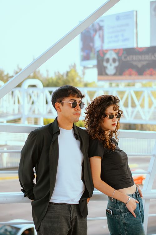 Free A fashionable pair of young adults wearing sunglasses pose stylishly outdoors on a sunny day. Stock Photo