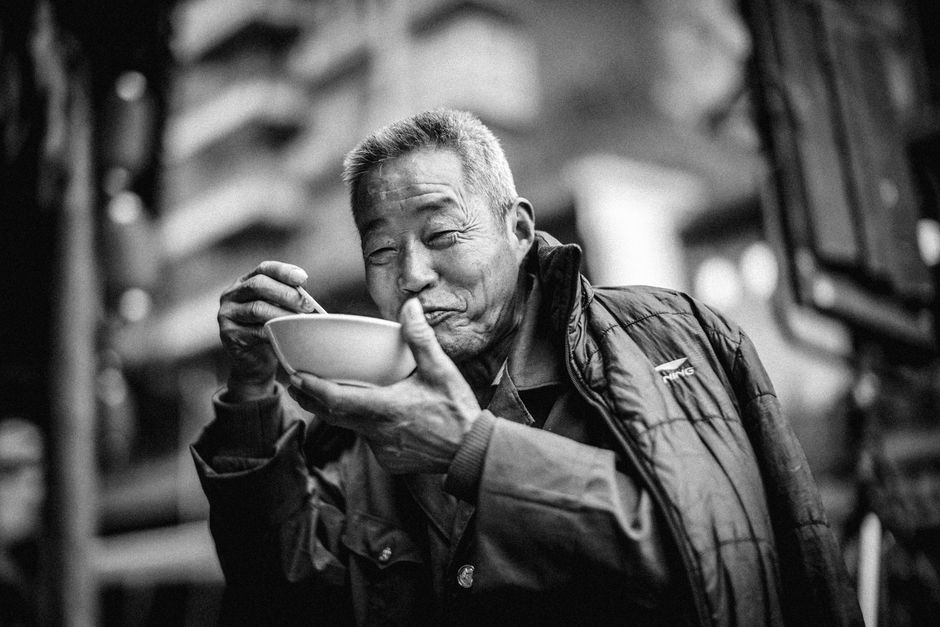 Black and white portrait of a smiling elderly man eating outdoors, evoking warmth and happiness.