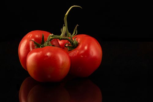 Free Vibrant red tomatoes arranged on a reflective black surface, showcasing freshness and natural beauty. Stock Photo