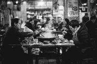 一张单色图像中，人们在繁忙的餐厅里用筷子吃饭