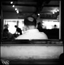 在灯光昏暗的咖啡馆里，一个成熟秃顶男人的背影被用黑白方式拍摄下来