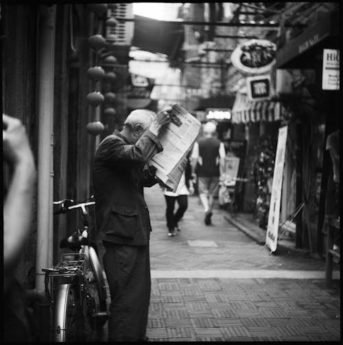 Grayscale Photo of Person Standing While Holding a Newspaper