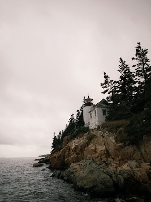 Scenic view of Bass Harbor Head Lighthouse perched on rugged cliffs along the Maine coastline on an overcast day.