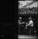 照片中，两名男子在户外酒吧享受谈话，这是一张黑白照片