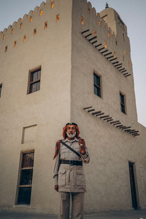 Free An Emirati man in traditional attire stands in front of a historical fort in Abu Dhabi. Stock Photo