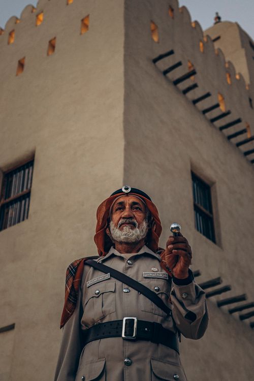 Free A traditional Emirati policeman stands in front of a historic fort in Abu Dhabi, highlighting UAE heritage. Stock Photo