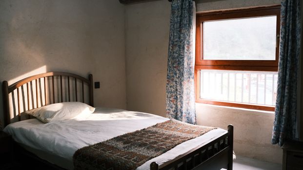 A tranquil bedroom with a wooden bed basking in natural sunlight through floral curtains.