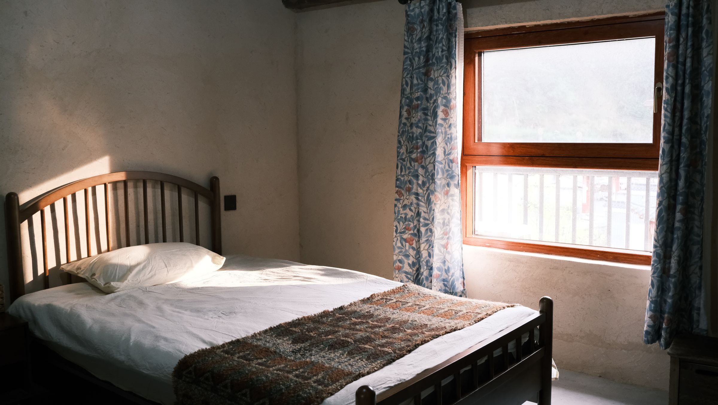 Sunlit bedroom with a red upholstered bed, floral curtains, white bedding and a timber nightstand