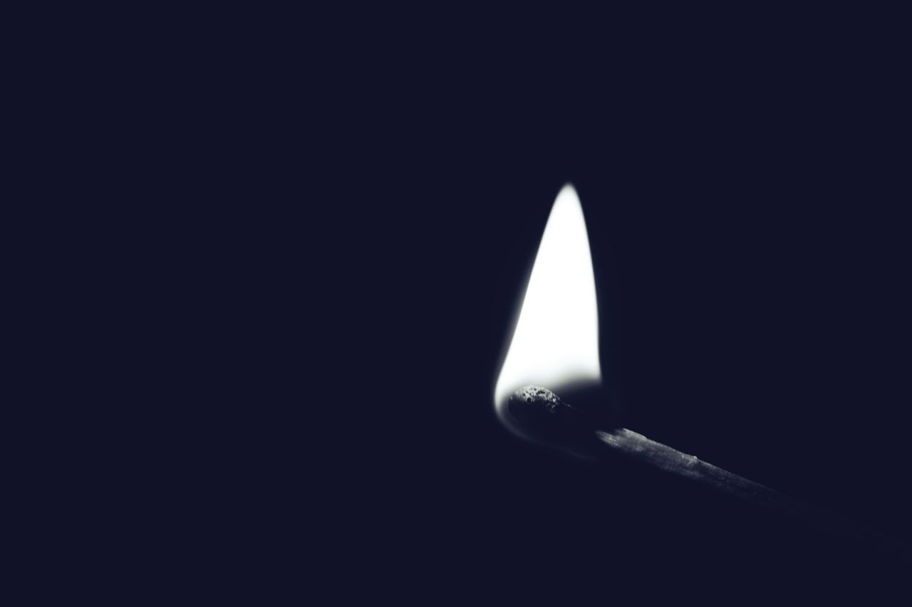 a minimalist black and white image of a lit matchstick with dark backg