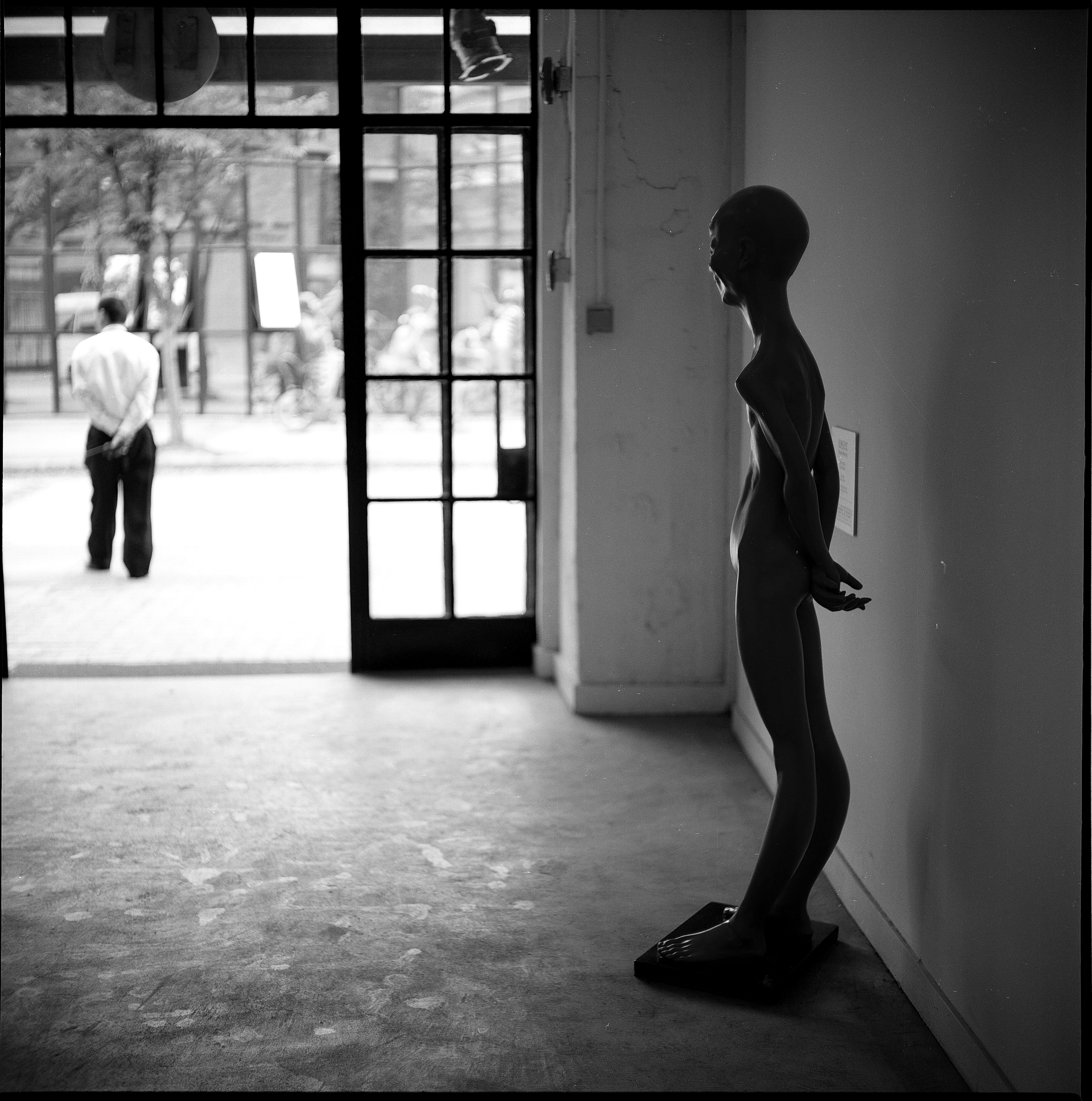 Black and white photo of a mannequin near a sunlit doorway, creating a dramatic silhouette indoors.