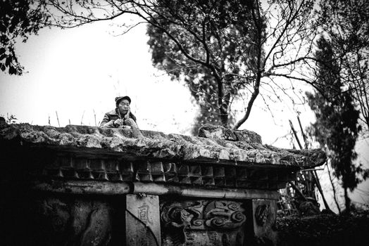 Black and white image of a person in a hat on an ornate stone structure with trees.