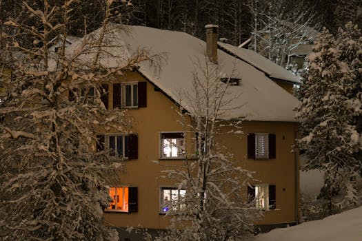 A quiet snow-covered house illuminated at night in a serene winter forest setting.