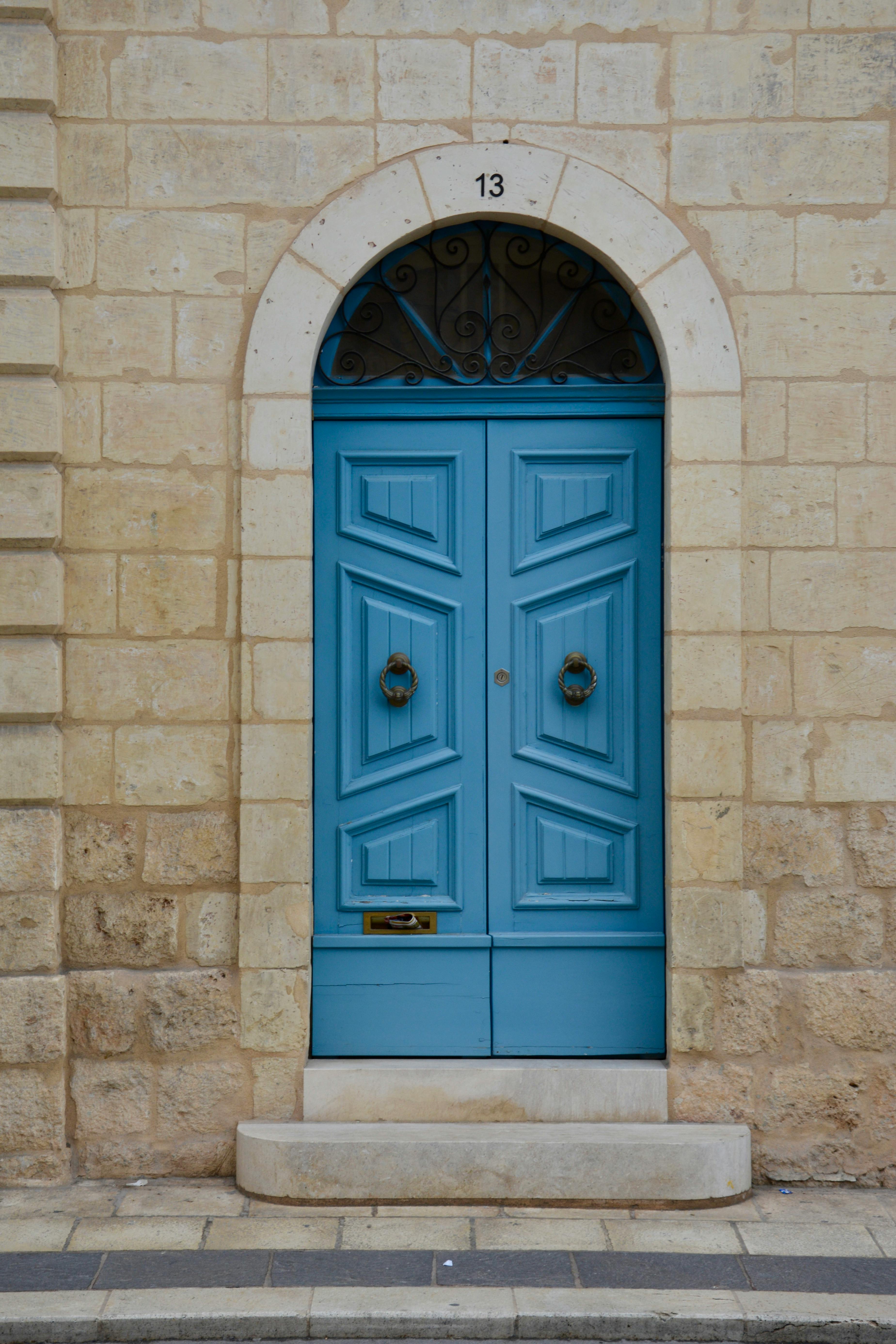 A vibrant blue door set in a historic stone archway in Malta, numbered 13.