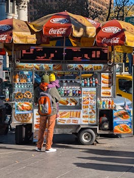A vibrant New York City street food cart with customers on a sunny day.