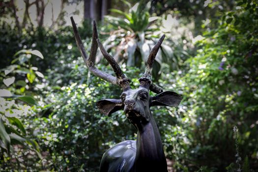 A striking deer statue amidst vibrant greenery in an outdoor garden.