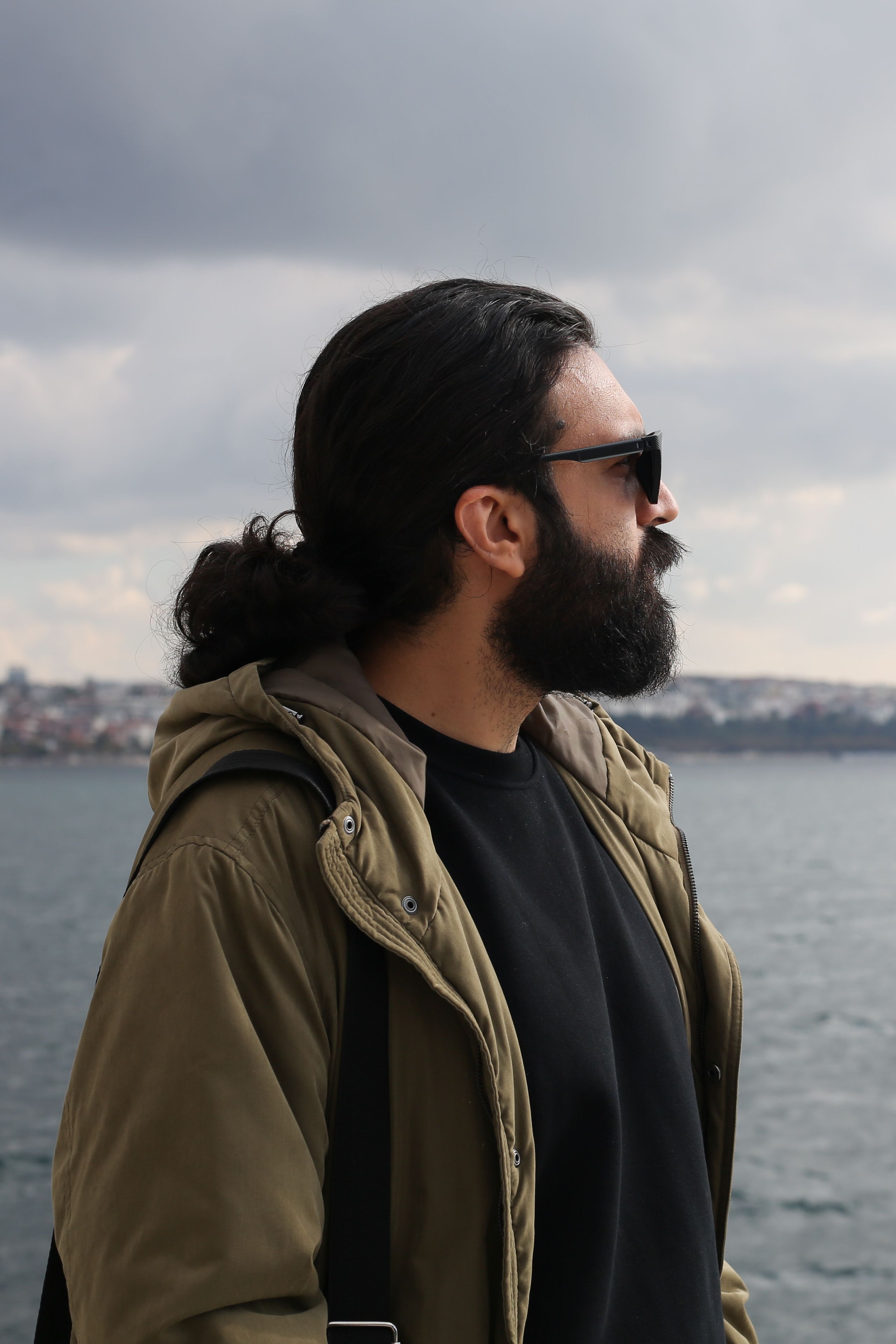 Outdoor portrait of a man with a beard and sunglasses by the Bosphorus in Istanbul, showcasing a trendy, modern look.