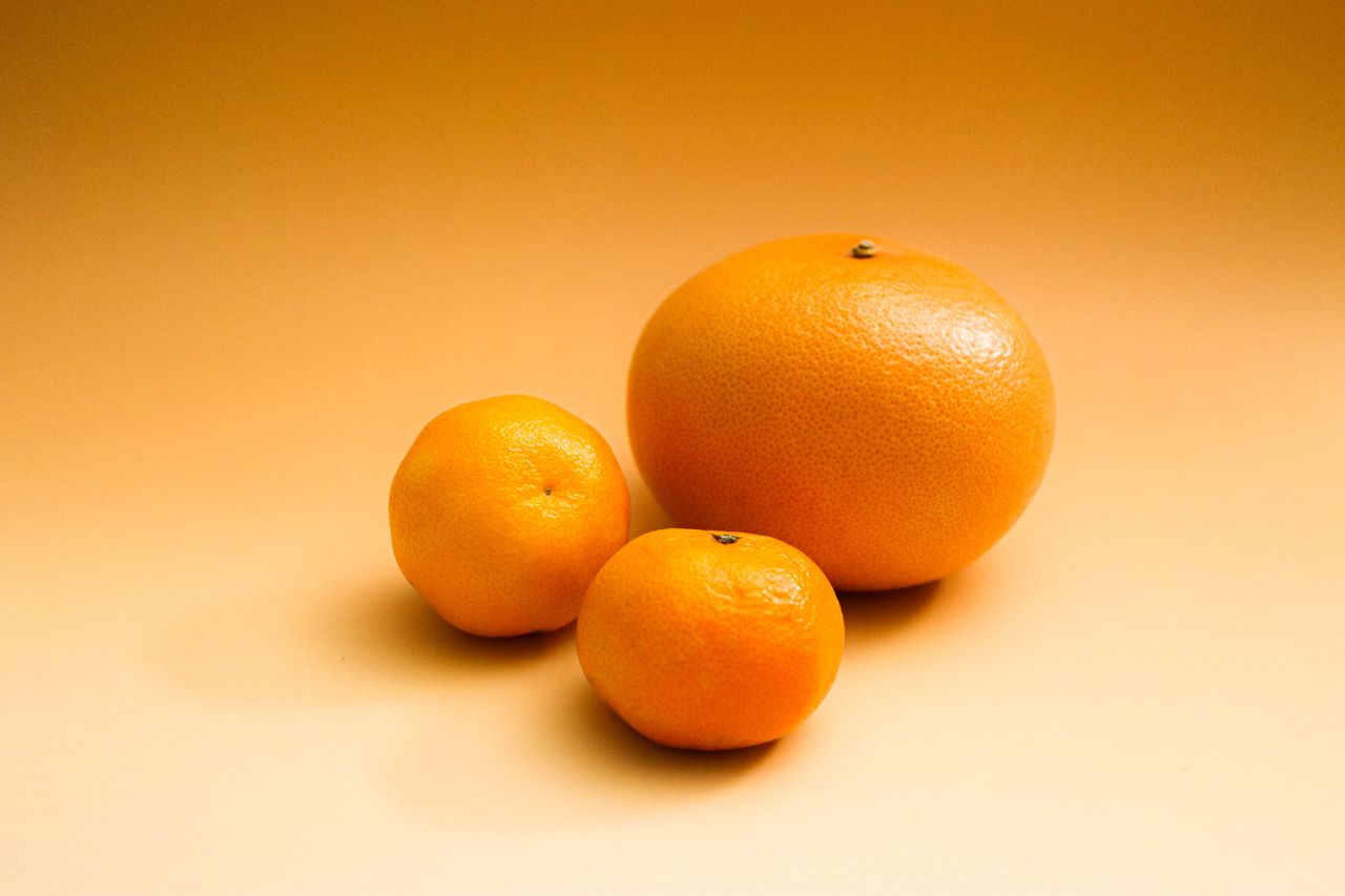 three citrus fruits including an orange and grapefruit on a gradient o