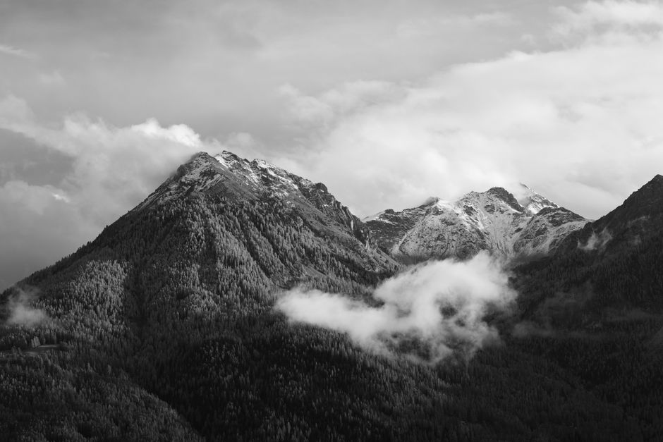 Stunning black and white photograph of snow-capped mountains under a cloudy sky.