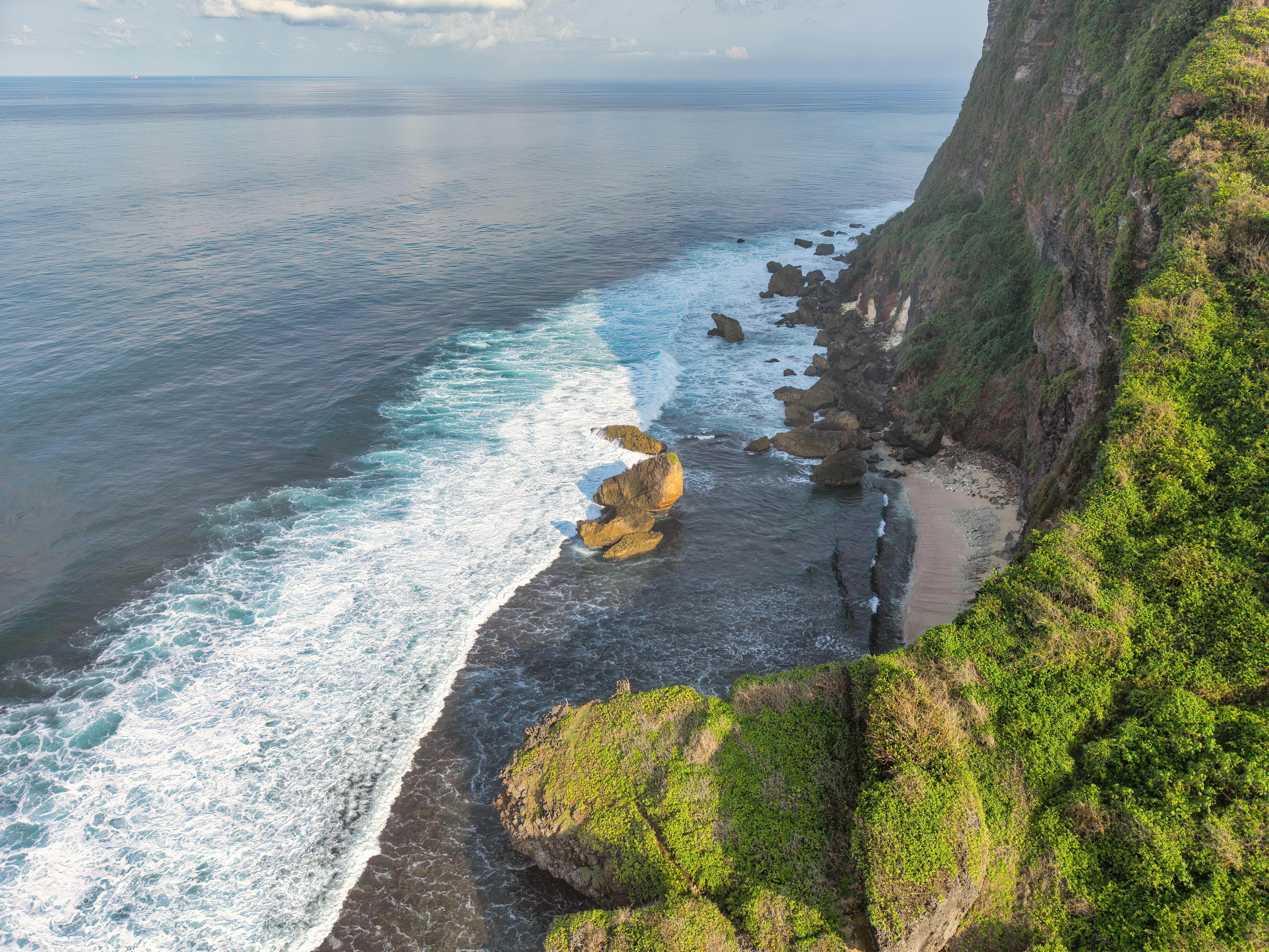 A mesmerizing aerial view of Bali's lush cliffs and the Indian Ocean's waves.
